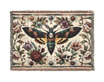May include: A tapestry throw blanket with a colorful moth and skull design. The moth is surrounded by flowers and vines, and the skull is at the bottom of the design. The background is a cream color with a grid pattern.