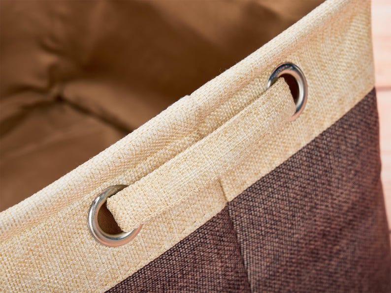 May include: Close-up of a beige and brown fabric storage bin with a drawstring closure. The bin has two metal grommets on the top edge.