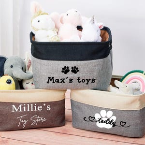 May include: Three gray canvas storage bins with black trim and paw print designs. The bins are labeled "Max's toys", "Millie's Toy Store", and "teddy".