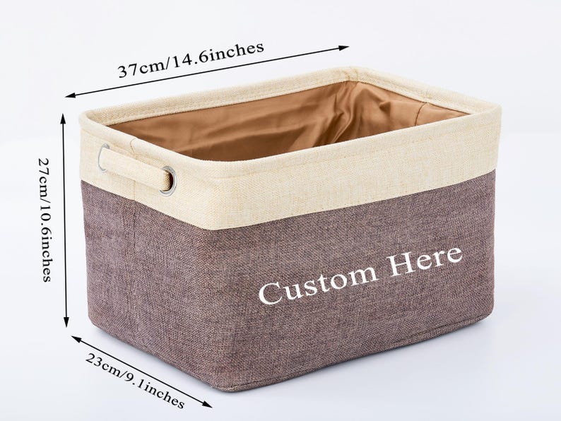 May include: A brown and beige fabric storage bin with a white handle and the text "Custom Here" printed on the front. The bin measures 14.6 inches wide, 10.6 inches tall, and 9 inches deep.