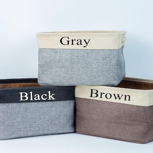 May include: Three fabric storage bins with black labels. The bins are gray, black, and brown. The labels read "Gray", "Black", and "Brown".