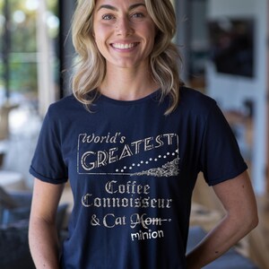 Peut inclure: T-shirt bleu marine avec l'inscription "World's Greatest Coffee Connoisseur & Cat Mom - minion" en blanc vieilli. Le t-shirt a des manches courtes et un col rond.