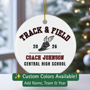 May include: A round white ceramic ornament with a gold hanging string. The design features the text TRACK & FIELD in dark red, a black winged running shoe graphic, the year 20 26, and the text COACH JOHNSON and CENTRAL HIGH SCHOOL in black.