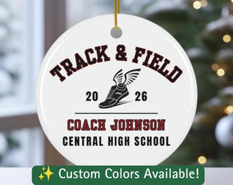 Puede incluir: Un adorno redondo de cerámica blanca con un cordón dorado para colgar. El diseño presenta el texto TRACK & FIELD en rojo oscuro, un gráfico de una zapatilla de correr alada en negro, el año 20 26 y el texto COACH JOHNSON y CENTRAL HIGH SCHOOL en negro.