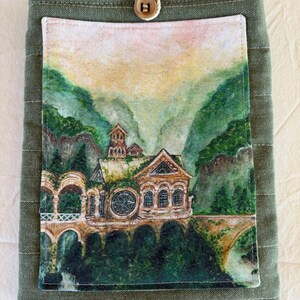 Op de afbeelding: Groene stoffen boekomslag met een aquarel schilderij van een gebouw in een berglandschap. De omslag heeft een knoopsluiting. De schildering toont een gebouw met boogvensters en een brug.