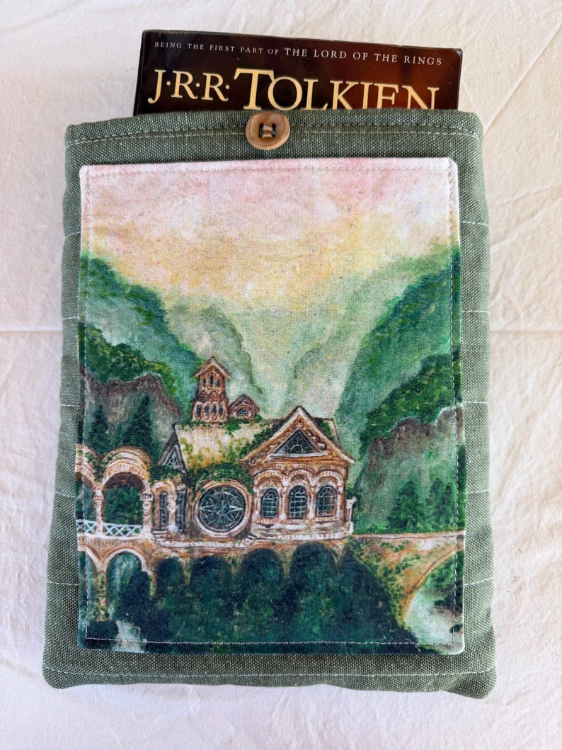 Op de afbeelding: Groene stoffen boekomslag met een knoopsluiting. De voorkant heeft een aquarel schilderij van een gebouw in een berglandschap. De boekomslag bevat een exemplaar van "The Lord of the Rings" van J.R.R. Tolkien.