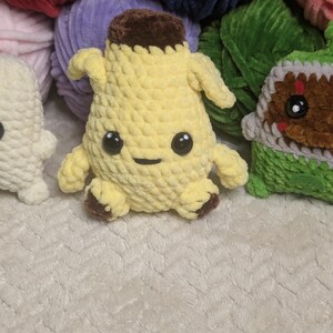 Pu&ograve; includere: Un peluche a forma di banana realizzato all'uncinetto, di colore giallo con la parte superiore e i piedini marroni. Il pupazzo presenta due piccole braccia, una bocca ricamata semplice e due grandi occhi di sicurezza in plastica nera.