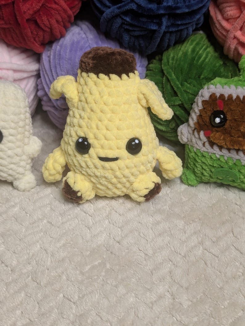 Pu&ograve; includere: Un peluche a forma di banana realizzato all'uncinetto, di colore giallo con la parte superiore e i piedini marroni. Il pupazzo presenta due piccole braccia, una bocca ricamata semplice e due grandi occhi di sicurezza in plastica nera.