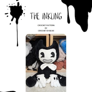 Pode incluir: Pelúcia de crochê preta e branca de um personagem de desenho animado com o texto "The Inkling" e "Crochet Pattern by Crochet by Bear". A pelúcia tem um rosto sorridente, luvas brancas e uma gravata borboleta branca.