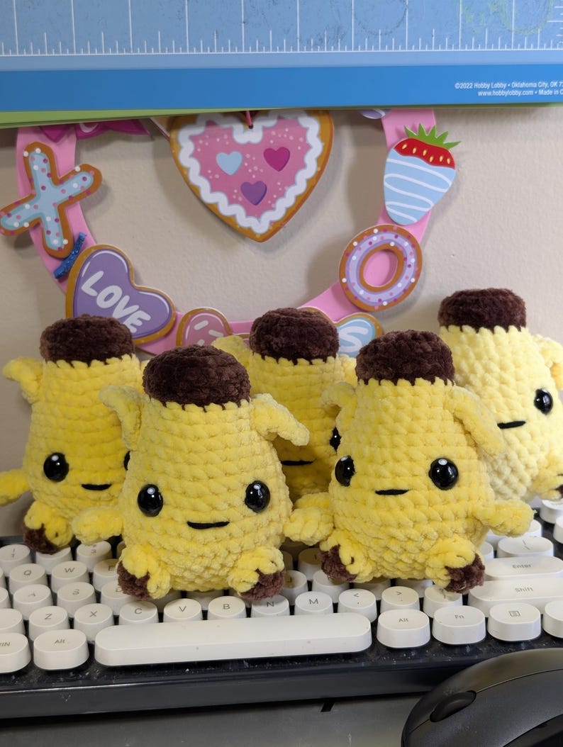 Pu&ograve; includere: Un gruppo di cinque piccoli peluche realizzati a mano all'uncinetto a forma di banana. Ogni peluche presenta un corpo giallo brillante, una parte superiore e inferiore marrone scuro, due occhi di sicurezza in plastica nera e una bocca ricamata.