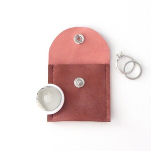 May include: A small, two-toned leather pouch with a snap closure. The pouch is pink on the top and brown on the bottom. Two silver rings are next to the pouch.
