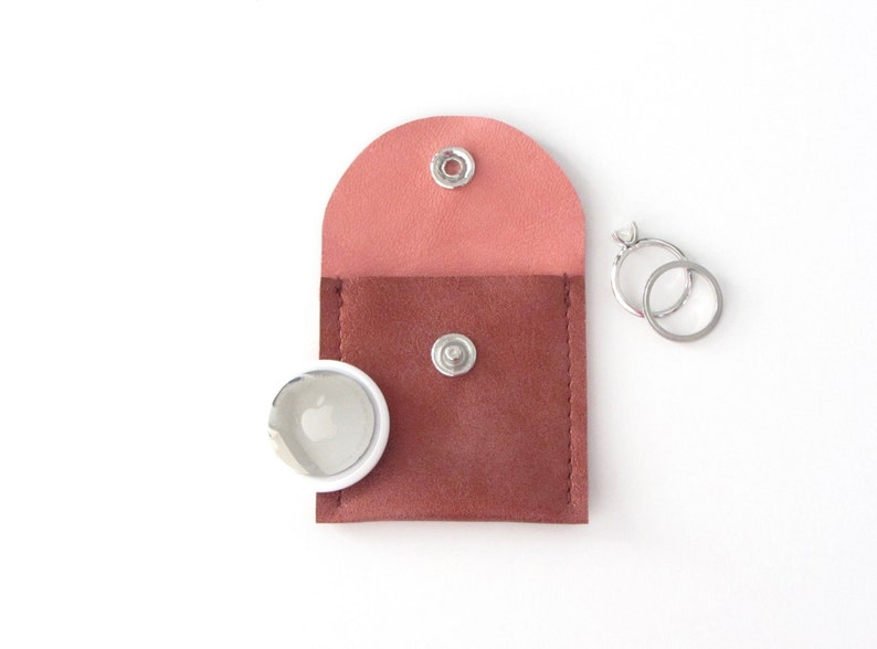May include: A small, two-toned leather pouch with a snap closure. The pouch is pink on the top and brown on the bottom. Two silver rings are next to the pouch.