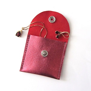 May include: A small red leather pouch with a snap closure, containing a gold necklace with a red gemstone pendant and a pair of gold earrings with red gemstones.