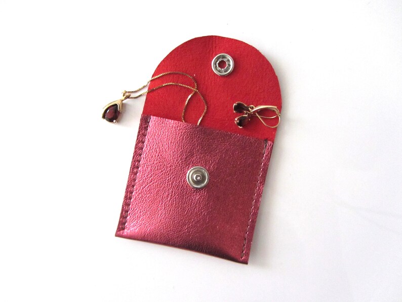 May include: A small red leather pouch with a snap closure, containing a gold necklace with a red gemstone pendant and a pair of gold earrings with red gemstones.