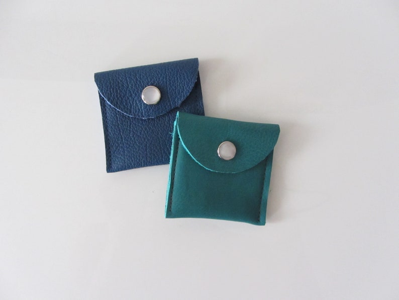 Puede incluir: Dos peque&ntilde;as bolsas de cuero con cierre de presi&oacute;n. Una bolsa es azul y la otra es turquesa.