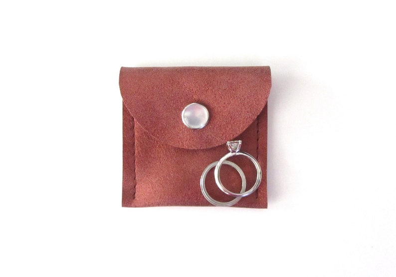 May include: A small brown leather pouch with a snap closure, containing two silver rings. One ring has a small diamond.