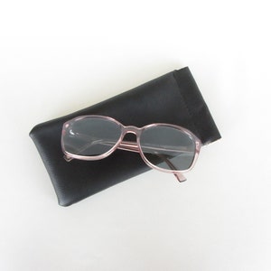 May include: A pair of pink sunglasses with dark lenses in a black leather case.