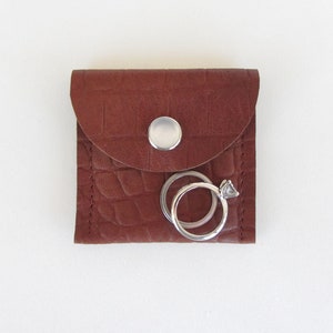 May include: A brown leather ring box with a snap closure and two silver rings inside.
