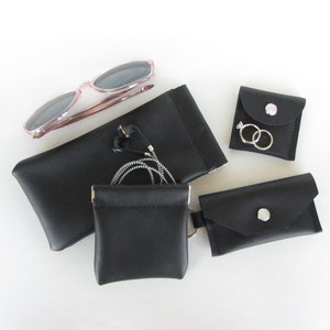 May include: An assortment of small black leather pouches and cases. Includes a glasses case, a small coin purse, and two small snap-closure pouches. A pair of sunglasses and earbuds are also visible.