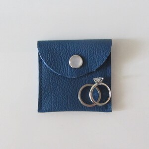Puede incluir: Una peque&ntilde;a caja de anillos de cuero azul con cierre de bot&oacute;n blanco. Dos anillos de plata est&aacute;n dentro de la caja.