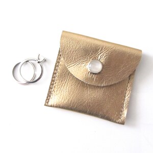 May include: Two silver rings in a gold leather ring box with a white button closure.