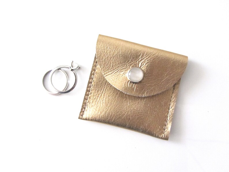 May include: Two silver rings in a gold leather ring box with a white button closure.