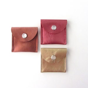 May include: Three small leather pouches with snap closures. The pouches are in shades of pink, brown, and gold.