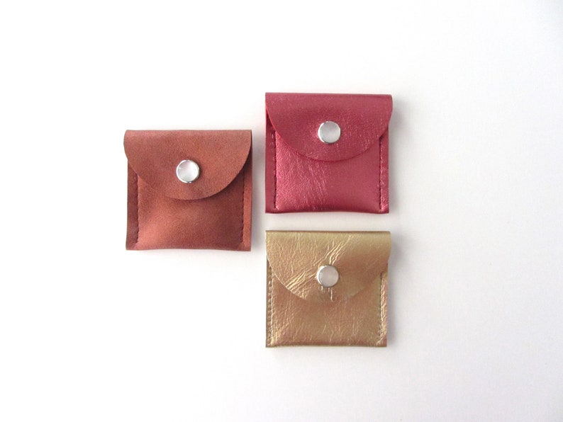 May include: Three small leather pouches with snap closures. The pouches are in shades of pink, brown, and gold.
