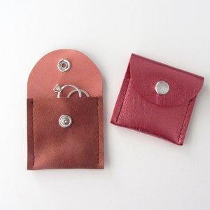 May include: Two small, pink leather pouches with snap closures. One pouch has a ring inside.