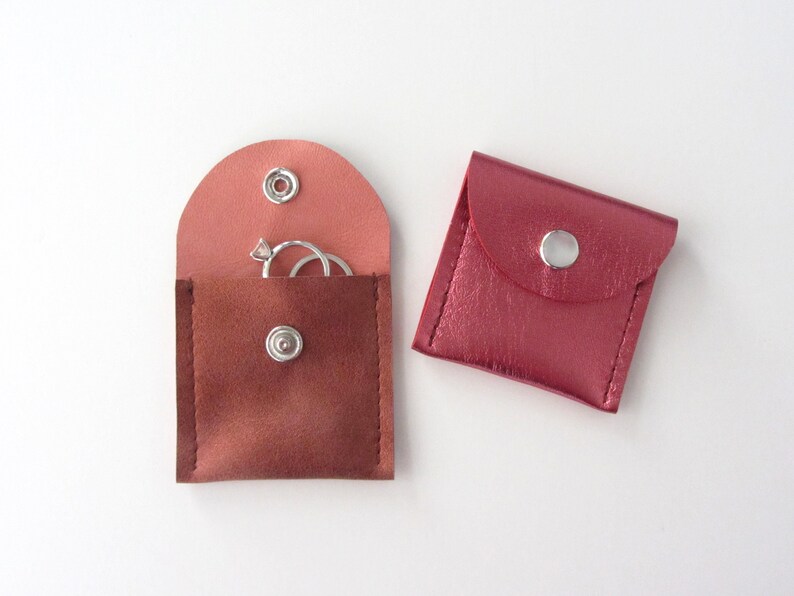 May include: Two small, pink leather pouches with snap closures. One pouch has a ring inside.