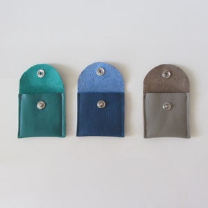 Puede incluir: Tres peque&ntilde;as carteras de monedas de cuero en color turquesa, azul y gris. Cada cartera tiene un cierre de presi&oacute;n.