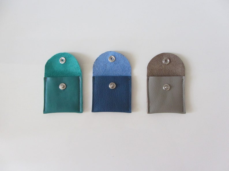 Puede incluir: Tres peque&ntilde;as carteras de monedas de cuero en color turquesa, azul y gris. Cada cartera tiene un cierre de presi&oacute;n.