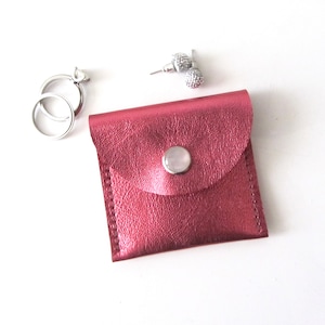 May include: A small, pink leather pouch with a snap closure. The pouch is ideal for storing small items like jewelry.