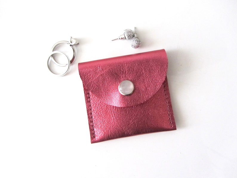 May include: A small, pink leather pouch with a snap closure. The pouch is ideal for storing small items like jewelry.
