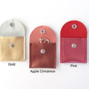 May include: Three small, square-shaped pouches with snap closures. The pouches are made of faux leather and come in gold, apple cinnamon, and pink.