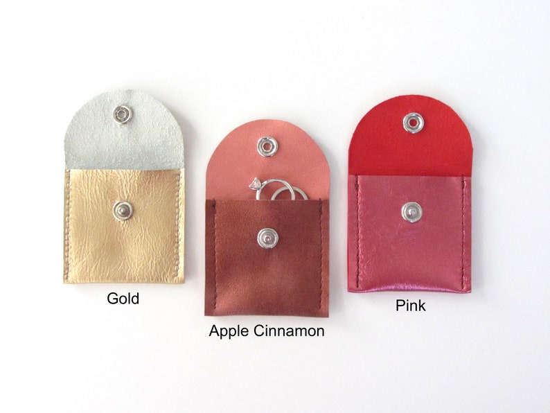 May include: Three small, square-shaped pouches with snap closures. The pouches are made of faux leather and come in gold, apple cinnamon, and pink.