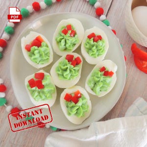 Puede incluir: Un plato blanco con seis huevos rellenos cubiertos con una mezcla de aguacate verde y trozos de pimiento rojo. El plato está sobre una superficie de madera con una guirnalda blanca y verde.