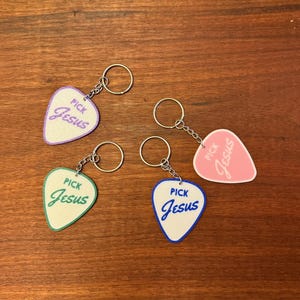 May include: Four guitar picks with keychains. Each pick has the words "Pick Jesus" written on it. The picks are purple, pink, green, and blue.