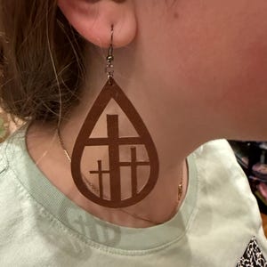 May include: Brown leather teardrop shaped earrings with a cutout design of three crosses.
