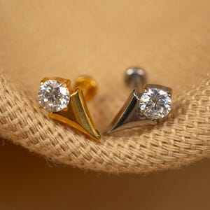 May include: Two nose rings with a pointed design and a clear gemstone. One ring is gold and the other is silver.