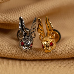 May include: A pair of rabbit-shaped earrings with red gemstone eyes. One earring is silver and the other is gold.