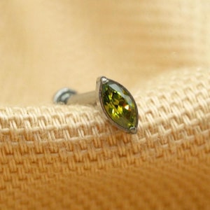May include: A green marquise-shaped gemstone set in a silver body piercing.