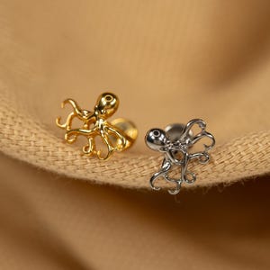 May include: Two octopus shaped body jewelry pieces. One is gold and the other is silver.