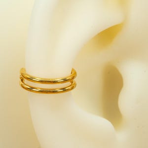 以下が含まれることがあります： 耳のピアス用のゴールドのダブルフープイヤリング。フープは2本の薄い金属バンドでできています。