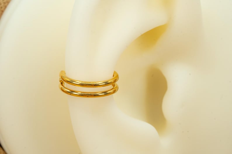 以下が含まれることがあります： 耳のピアス用のゴールドのダブルフープイヤリング。フープは2本の薄い金属バンドでできています。