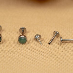 Puede incluir: Cinco piezas de joyer&iacute;a corporal plateadas con acentos de piedras preciosas verdes. Dos son pendientes de bot&oacute;n, una es una barra y dos son postes.