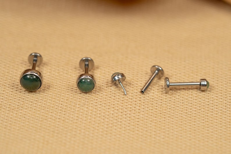 Puede incluir: Cinco piezas de joyer&iacute;a corporal plateadas con acentos de piedras preciosas verdes. Dos son pendientes de bot&oacute;n, una es una barra y dos son postes.
