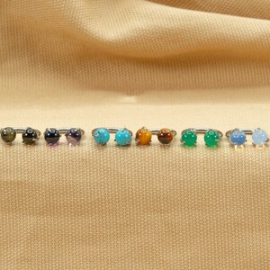 May include: A row of 10 silver rings with different colored gemstones. The gemstones are turquoise, amethyst, tiger's eye, black onyx, green jade, and blue agate.