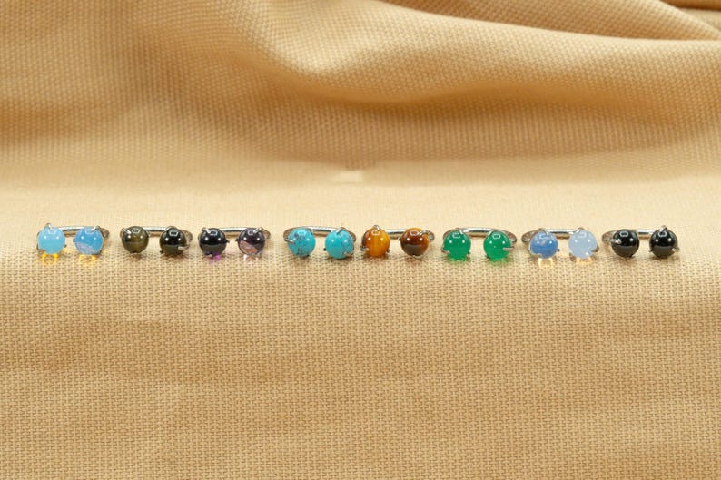 May include: A row of 10 silver rings with different colored gemstones. The gemstones are turquoise, amethyst, tiger's eye, black onyx, green jade, and blue agate.