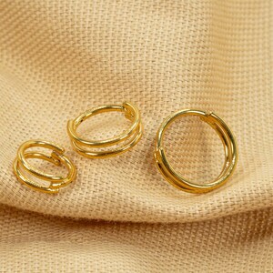 以下が含まれることがあります： 異なるサイズの3つの金のフープイヤリング。イヤリングは、2つの細いフープで構成されています。